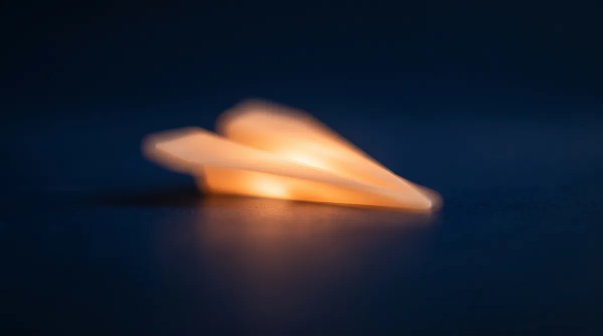 A glowing orange paper-plane-shaped light form at rest on a dark navy surface